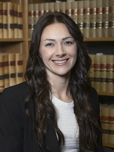 Woman longer brown hair smiling in black blazer in front of shelves of law books